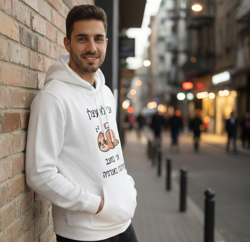 תמונת אווירה המציגה גבר צעיר ומחייך לובש קפוצ'ון (Hoodie) לבן בעיצוב אישי, עם איור הומוריסטי של דוב נמלים ישן והכיתוב: "אני לא עצלן, אני במצב חיסכון באנרגיה" – דוגמה להדפסה על ביגוד בהראל צלמים קרית אתא